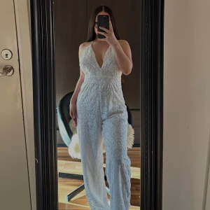 Vit långklänning från Bik Bok - Elegant vit långklänning från Bik Bok med v-ringad hals och vackert broderat mönster. Klänningen har en stilren design och är perfekt för speciella tillfällen. Den är ärmlös och har en smickrande passform.🥰🥰🥰