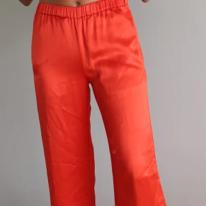 Röda vida byxor från Carin Wester, strlk 34  - Snygga röda byxor med elastisk midja och vida ben. Perfekta för en avslappnad stil med en touch av färg. Byxorna har en slät yta och är bekväma att bära.