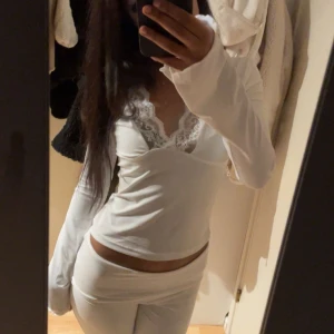 Vit långärmad topp med spetsdetaljer - Säljer en stilren vit långärmad topp med v-ringad spetsdetalj vid halsen. Perfekt för en elegant och bekväm look. Passar bra till både jeans och kjol. Hör av dig vid intresse!