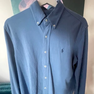 Ralph Lauren skjorta  - Snygg blå skjorta från Ralph Lauren med klassisk krage och knappar framtill. Skjortan har en broderad logotyp på bröstet och är långärmad. Perfekt för en stilren look i storlek M. Skick 9/10✅ Skriv vid frågor eller funderingar i DM🍾