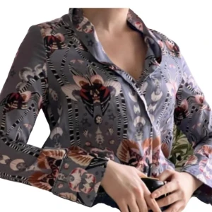 Mönstrad blus från By Malina - Säljer en elegant mönstrad blus från By Malina i en mix av grå, rosa och beige toner. Blusen har långa ärmar och ett unikt mönster med blommor och geometriska former. Perfekt för att ge en färgklick till din garderob!