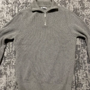 Grå stickad half zip tröja från Zara  - Snygg grå stickad tröja från Zara med halv dragkedja och ribbade detaljer. Perfekt för kyligare dagar med sin stilrena design och bekväma passform.