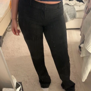 Svarta randiga byxor från Madlady - Snygga svarta byxor från Madlady med diskreta ränder. Byxorna är i deras lågmidjade modell och en rak passform som ger en stilren look. Perfekta för en chic och modern stil. Har lite slitningar längst ner vid fötterna. 