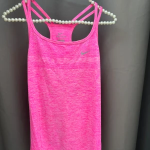 Rosa linnetopp från Nike - Säljer en snygg rosa linnetopp från Nike med Dri-FIT-teknologi. Perfekt för träning med sin lätta och andningsbara design. Den har smala axelband och en sportig look🩷