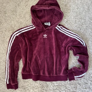 Vinröd hoodie från Adidas - Säljer en snygg vinröd hoodie från Adidas. Den är i Velour / Plysch / Velvet material och storleken är 32 men den är mer en xs-s.