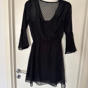 Svart glitter prickig klänning - Snygg svart klänning med prickigt glitter mönster och omlott-design. Klänningen har trekvartsärmar och en v-ringad hals. Lapp finns ej kvar men skulle uppskatta den till storlek xs/s (katt och kanin finns i hemmet)