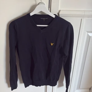 Mörkblå tröja från Lyle & Scott - Säljer en stilren mörkblå tröja från Lyle & Scott med v-ringning och ett broderat gult emblem på bröstet. Tröjan är i princip helt ny! OBS!!! Det är i barnstorlek S