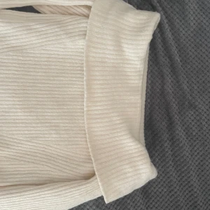Beige ribbad offshoulder tröja - Säljer en stilren beige ribbad tröja från H&M. Tröjan har en offshoulder-design och långa ärmar, perfekt för en chic look. Den mjuka ribbade texturen ger en skön känsla och en snygg passform. Använt bara en gång.