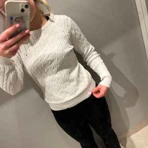 Gant tröja - Säljer en stilren vit stickad tröja från Tommy Hilfiger med kabelstickat mönster. Tröjan har långa ärmar och en rund halsringning. Perfekt för en klassisk och bekväm look. Den har ett märke vid axeln se bild tre❤️