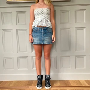 Vit och blå prickig tubtopp från Zara - Säljer en söt vit tubtopp från Zara med blå prickar och volangdetalj i nederkant. Perfekt för sommardagar och kan enkelt matchas med jeans eller kjol. Toppen är ärmlös och har en smickrande passform.