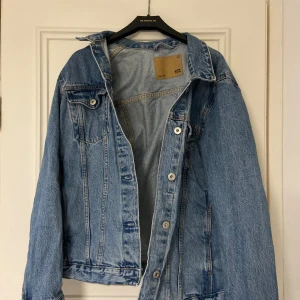 Blå jeansjacka från 157 - Säljer en klassisk blå jeansjacka från 157. Jackan har en normal passform med knappar framtill och två bröstfickor med lock. Perfekt för vår och sommar!