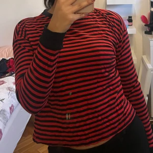 Röd och svart randig tröja - Säljer en röd och svart randig tröja med långa ärmar och svarta muddar. Perfekt för en avslappnad stil. Passar bra till jeans eller kjol.