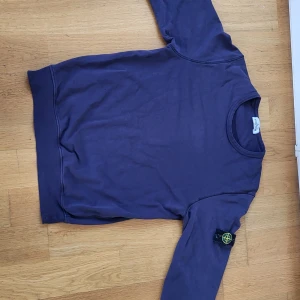 Stone Island tröja - Säljer en snygg lila tröja från Stone Island med deras ikoniska märke på ärmen. Tröjan har en klassisk rund hals och är perfekt för en stilren look. Den är tillverkad i ett mjukt material som känns skönt mot huden.