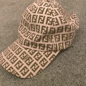 Fendi keps  - Snygg keps i beige och brun med ett iögonfallande logotypmönster. Perfekt för att ge din outfit en trendig touch. Justerbar passform för extra komfort.