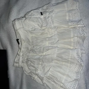 Vit kjol från Diverse -  vit kjol från Diverse med  spetsdetaljer och volanger. Den har en justerbar midja. 