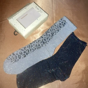 Glittriga strumpor från ICHI - Säljer ett par glittriga strumpor från ICHI. Ena paret är grått med leopardmönster och det andra är svart med glitter. Perfekta för att ge lite extra stil till din outfit. Kommer i originalförpackning.