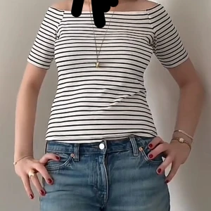 Randig offshoulder topp - Säljer en vit och svart randig offshoulder topp med korta ärmar. Toppen har en smickrande passform och är perfekt att matcha med jeans eller kjol. Enkel och stilren design som passar till många tillfällen.