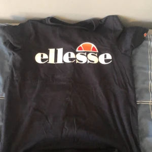 Svarta mjukisbyxor från Ellesse - Adlrig använt. Svarta mjukisbyxor från Ellesse med stort vitt tryck längs ena benet och liten logga vid fickan. Byxorna har resår och snörning i midjan samt muddar vid bensluten. Perfekta för en avslappnad stil.