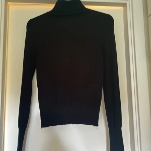 Svart polotröja i stickat material - En klassisk svart polotröja i stickat material med lång ärm och tight passform. Perfekt att styla till olika outfits och funkar året runt. Polokragen ger en stilren look. Lappen är borta men den är från Nelly