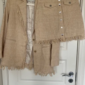 Beige kostym med kjol och kavaj från Rodebjer med fransdetaljer - Beige Rodebjer kavaj och kjol sett, kan säljas separat. Tillsammans 5500kr, kavajen är ursprungligen 5500kr och kjolen 2700kr.