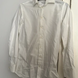 Vit skjorta från Selected Homme - Klassisk vit skjorta från Selected Homme i slim fit-modell. Skjortan har långa ärmar, knappar framtill och en stilren krage. Perfekt för dig som vill ha en enkel och stilren look.