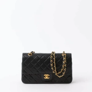 Svart quiltad handväska  - Klassisk svart handväska  i quiltat skinn med guldfärgade metalldetaljer och kedjerem. Väskan har ikonisk CC-lås framtill och en ficka på baksidan. Perfekt accessoar för att lyfta din stil.