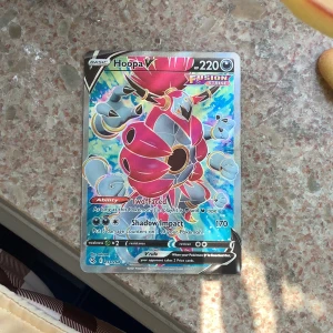 Pokémonkort Hoopa V Fusion Strike - Säljer ett Pokémonkort av Hoopa V från Fusion Strike-serien. Kortet har holografisk yta och visar Hoopa i färgstarka rosa, blå och gula toner. HP 220 och attacken Shadow Impact. Perfekt för samlare eller Pokémon-fans!