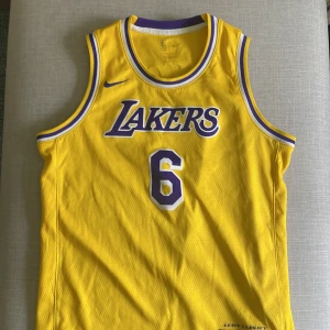 Gul Lakers baskettröja LeBron James #6 - Säljer en gul Los Angeles Lakers baskettröja från Nike med LeBron James och nummer 6. Tröjan har lila och vita detaljer runt krage och ärmhål samt Lakers-logga på bröstet. Perfekt för basketfans som vill sticka ut på match eller träning.