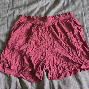 Vinröda shorts med resårmidja - Säljer ett par vinröda shorts med resår i midjan och lös passform. De är tillverkade i ett lätt, skrynkligt tyg som känns luftigt och bekvämt. Perfekta för varma dagar och enkel att matcha med olika toppar.