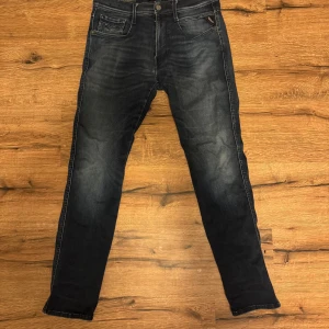 Mörkblå Replay Anbass jeans - Säljer ett par mörkblå Replay Anbass jeans i storlek W31 L30. Jeansen har klassisk femficksdesign, smal passform och snygga slitningar längs benen. Perfekta för dig som gillar en modern och stilren look.