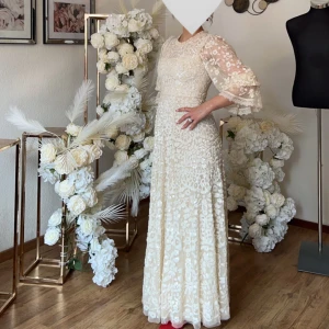 Vit långklänning med spets och blommigt mönster - Benvit långklänning med blommigt spetsmönster och  puffärmar. Klänningen har rund halsringning och vackra detaljer över hela tyget, perfekt för speciella tillfällen som t.ex fester eller bal. Köpt för 10 000kr och har endast använts vid två tillfällen och är därav i nytt skick. Skriv vid andra frågor.