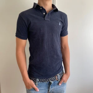 Mörkblå Pike från Polo Ralph Lauren - Säljer en mörkblå pikétröja från Polo Ralph Lauren med broderad logga på bröstet. Perfekt inför sommaren! 🏖️ Tröjan är i Slim Fit model i storlek S. Modellen är 178cm lång. Tveka inte på att skriva om du har funderingar!🤩 Priset är inte hugget i sten 🪨 