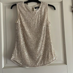 Glittrig ärmlös topp från ChicMe - Säljer en superfin glittrig ärmlös topp från ChicMe i ljusbeige med massor av paljetter. Perfekt för att sticka ut på festen! Rund halsringning och knapp i nacken för enkel påklädning.