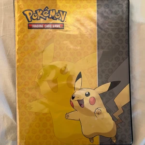 Pokémon Trading Card Game samlarpärm med Pikachu-omslag - Säljer en Pokémon samlarpärm med Pikachu-motiv på omslaget. Pärmen innehåller flera sidor med Pokémonkort i plastfickor, bland annat kort från olika generationer och energikort. Perfekt för dig som vill organisera och visa upp din samling.