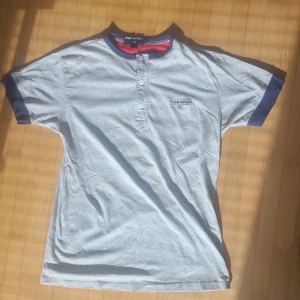 Ljusblå t-shirt från Polo Sport Ralph Lauren - Säljer en snygg och stilren Polo Sport T-shirt i ljusgrå färg med blåa detaljer – perfekt inför sommaren! Tröjan har en sportig design med knappar vid halsen och ett diskret broderat Polo Sport-märke med amerikansk flagga på bröstet. Den är i mycket bra begagnat skick och passar både till vardags och för sommarens alla tillfällen. Nypris ca 799 kr, jag säljer den nu för endast 299 kr – ett riktigt kap!  