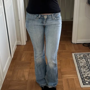 Ljusblå bootcut jeans - Säljer ett par ljusblå lågmidjade jeans med bootcut passform och klassisk femficksdesign. Finns viss slitage på jeansen, exempelvis längst ner vid fötterna och vid skrevet. Hör av dig för fler bilder eller frågor. Midjemått rakt över - 36 cm    Innerbenslängd- 83 cm