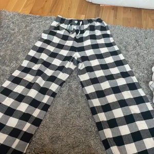 Svartvita rutiga byxor från H&M - Säljer ett par svartvita rutiga byxor från H&M med resår i midjan och snörning. Byxorna har en loose passform och är perfekta för en avslappnad stil. Tillverkade i mjuk bomull för extra komfort.