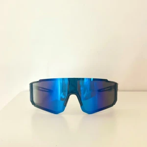 Snygga sportiga solglasögon  - Säljer ett par sportiga solglasögon med blått spegelglas och svart båge. Glasögonen har en modern, kantig form och bred lins som ger bra täckning😎 Perfekta för dig som gillar en futuristisk look och vill sticka ut🔥