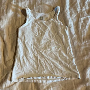 Vit linnetopp från Basic U - Säljer en enkel vit linnetopp från Basic U i mjuk bomull. Perfekt för varma dagar eller som lager under andra plagg. Klassisk passform med ärmlös design och rund halsringning.