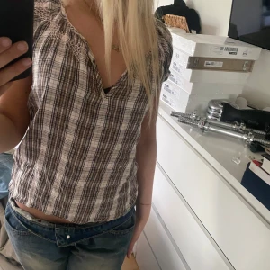 Brun och vit rutig blus med spetsdetaljer - Säljer en brun och vit rutig blus med korta ärmar och v-ringning. Blusen har fina spetsdetaljer vid axlarna och en avslappnad passform. Perfekt till jeans eller kjol för en avslappnad look. Jätte mysig att ha till sommaren!🌸💘💘