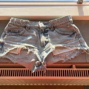 Ljusblå jeansshorts från Gina Tricot - Snygga ljusblå jeansshorts från Gina Tricot med fransiga benslut och slitna detaljer framtill. Klassisk femficksmodell med knapp och dragkedja. Perfekta för varma dagar och enkel att matcha med olika toppar. Väldigt korta där fram!