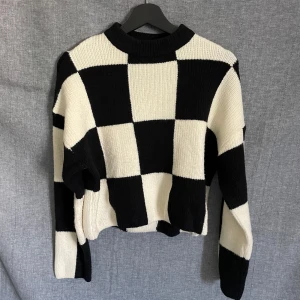 Svartvit stickad tröja med rutigt mönster - Säljer en stickad tröja med svartvitt rutigt mönster. Tröjan har lång ärm, rund halsringning och är perfekt för dig som gillar en trendig och iögonfallande stil.