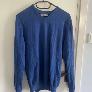 Blå bomullströja med v-ringning från Race Marine - Säljer en blå tröja från Race Marine, The Essentials, i ekologisk bomull. Tröjan har v-ringad hals och långa ärmar. Perfekt för lager-på-lager och enkel att matcha med olika outfits.