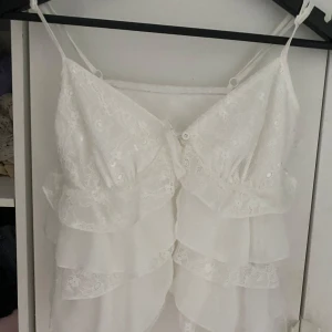 Vit spets topp med volanger - En topp med volanger. Det är 2 knappar men ett av snörerna är trasigt men kan fixa det innan jag säljer den om någon vill köpa annars aldrig använd 