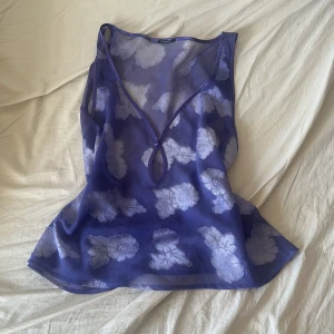 Lila blommig linnetopp med v-ringning s/ m - Säljer en lila, transparent linnetopp med vita blommor och v-ringning framtill. Toppen har ett litet nyckelhålsutskärning och är ärmlös. Perfekt för varma dagar! Vet ej märket 