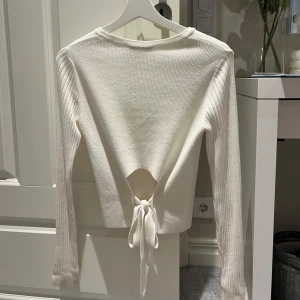 Vit finstickad tröja med knyt i ryggen - Säljer en vit finstickad tröja med lång ärm och snygg knytning i ryggen. Knappt använd så den är i väldigt bra skick 