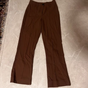 Bruna kostymbyxor med raka ben - Säljer ett par bruna kostymbyxor med raka ben och pressveck. Byxorna har normal passform och stängs med knapp och dragkedja. Från bershka