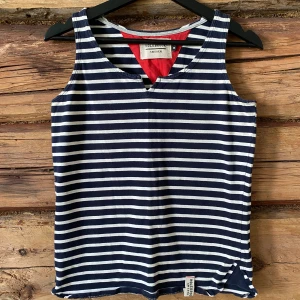 Randig linnetopp från Holebrook - Säljer en marinblå och vit randig linnetopp från Holebrook Sweden. Toppen är ärmlös med en liten v-ringning och har en klassisk, avslappnad passform. Perfekt för varma dagar och enkel att matcha med jeans eller shorts.