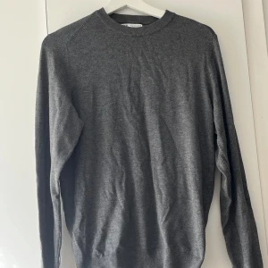 Grå stickad tröja - Säljer en enkel och stilren grå stickad tröja med rund halsringning. Tröjan har långa ärmar och är perfekt för lager-på-lager under kyligare dagar. Passar till det mesta och är ett måste i garderoben.