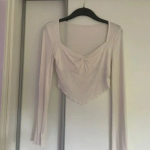 Vit långärmad topp med twistad detalj - Säljer en vit långärmad topp med snygg twistad detalj framtill och v-ringad hals. Toppen har en croppad passform, säljs då det inte är min stil längre! 